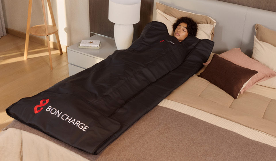 woman with eyes closed, in sauna blanket laying flat on a bed