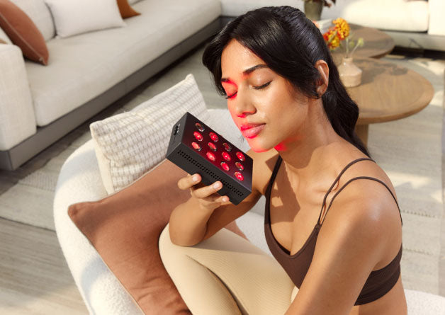 Woman holding up a handheld red light device to one side of face
