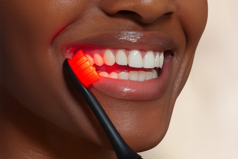 Close-up of a person using a red light toothbrush on their teeth.