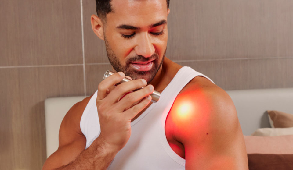 Man holding a Red Light Device applying it to an area of his shoulder