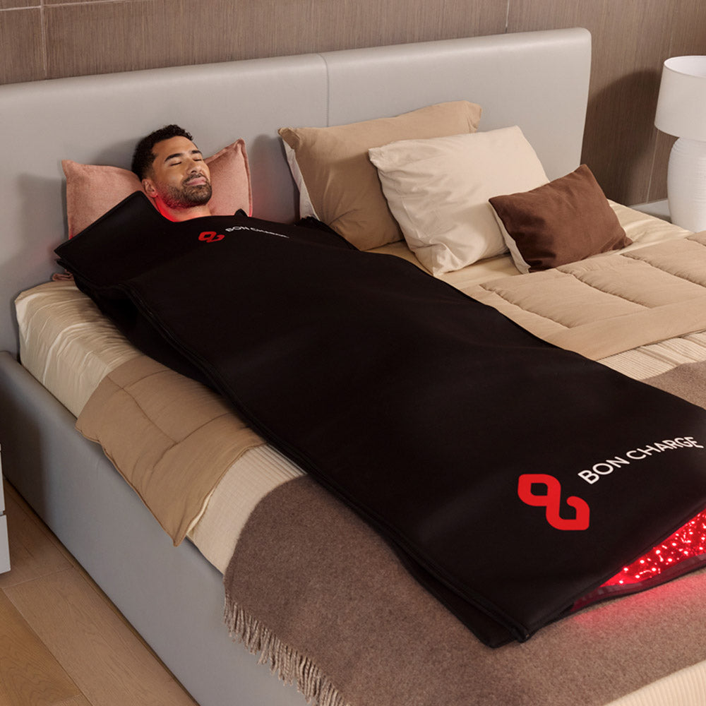 Man lying on a bed wrapped head to toe in the glowing red light blanket